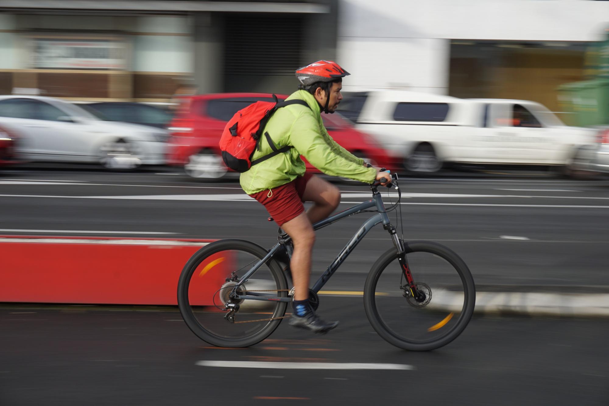 Man riding a bike in a road with cars behind him